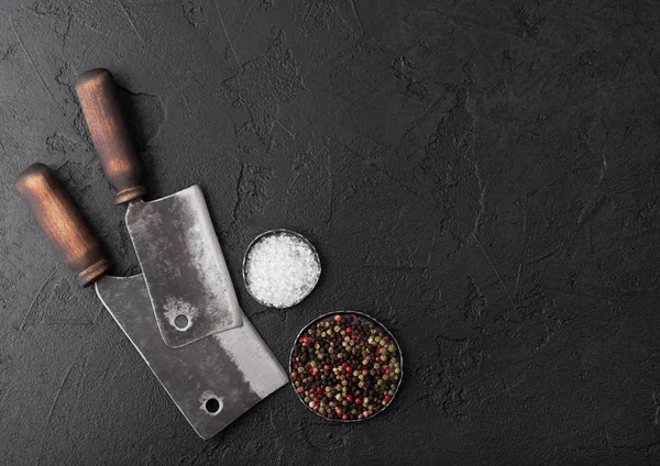 Vintage vlees mes bijlen op zwarte steen tabel achtergrond. Slager gebruiksvoorwerpen. Zout en peper. Ruimte voor tekst — Stockfoto