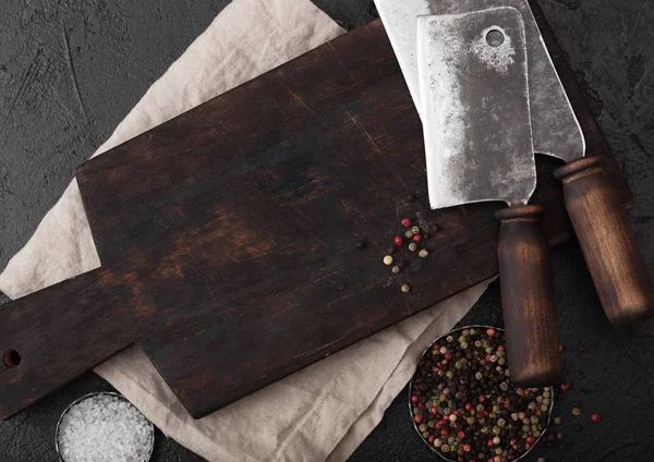 Coltello da carne vintage ascia su tagliere vintage e sfondo del tavolo in pietra nera. Utensili da macellaio. Sale e pepe . — Foto Stock