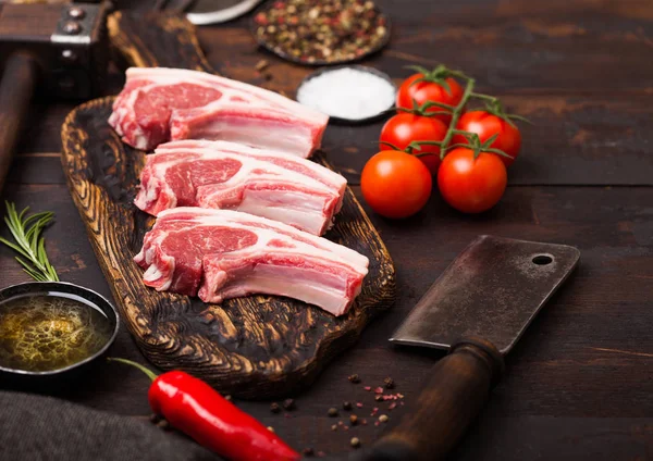 Fresh raw butchers lamb beef cutlets on chopping board with vintage meat hatchet and hammer on wooden background.Salt, pepper and oil with tomatoes and garlic and barbeque sauce. — Stock Photo, Image