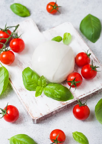 Fresh Mozzarella cheese on vintage chopping board with tomatoes and basil leaf on stone kitchen table background. — Stock Photo, Image