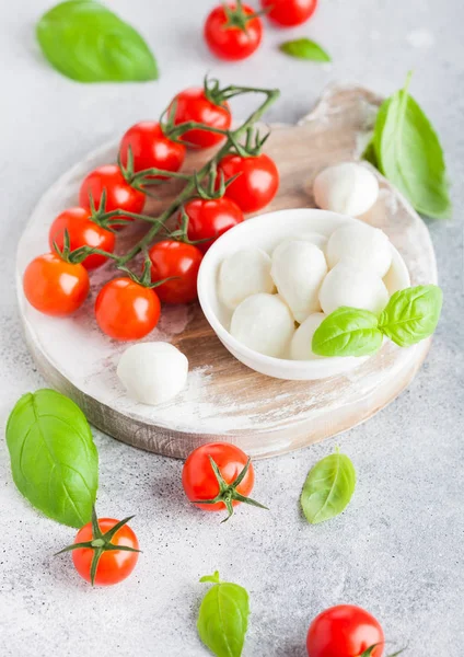 Fresh Mini Mozzarella cheese on vintage chopping board with tomatoes and basil leaf on stone kitchen table background. — Stock Photo, Image