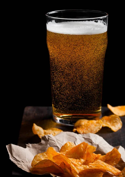 Glas pils bier met aardappel chips snack op vintage houten bord op zwarte achtergrond. Bier en snack. — Stockfoto