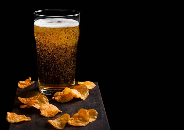 Vaso de cerveza lager con patatas fritas snack en tablero de madera vintage sobre fondo negro. Cerveza y merienda. Espacio para texto — Foto de Stock