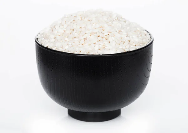 Black bowl of raw organic arborio risotto rice on white background. Healthy food. — Stock Photo, Image