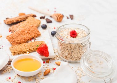 Çilek tatlım kaşık ve yulaf kavanoz ile mermer tahtada ve mermer zemin üzerine Hindistan cevizi ile organik tahıl granola bar. 