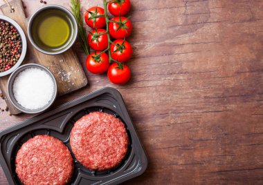 Baharat ve otlar ile ham kıyılmış ev yapımı sığır Burger ile plastik tepsi. Üst görünüm ve domates tuz ve biber ile ahşap mutfak masa arka plan üstünde metin için alan.