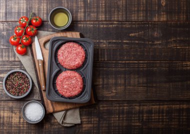 Baharat ve otlar ile ham kıyılmış ev yapımı sığır Burger ile plastik tepsi. Üst görünüm ve domates tuz ve biber ile ahşap mutfak masa arka plan üstünde metin için alan.