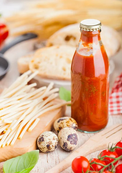 Σπιτικά μακαρόνια ζυμαρικά με αυγά ορτυκιού με μπουκάλι σάλτσα ντομάτας και τυρί σε ξύλινο υπόβαθρο. Το φαγητό κλασικό ιταλικό χωριό. Σκόρδο, μαύρο και πράσινες ελιές, λάδι και ψωμί. Τηγάνι — Φωτογραφία Αρχείου