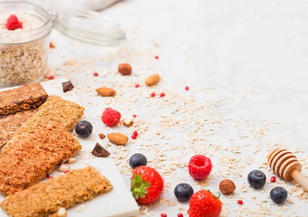 Barra de granola de cereales ecológicos con bayas sobre tabla de mármol con cuchara de miel y tarro de avena y toalla de lino sobre fondo de mármol . — Foto de Stock