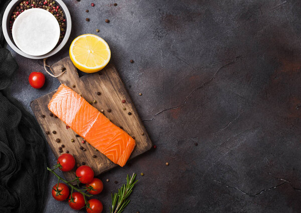 Свежий сырой ломтик лосося на доске с помидорами перца и лимоном на каменном кухонном столе. Пространство для текста. С розмарином и солью
