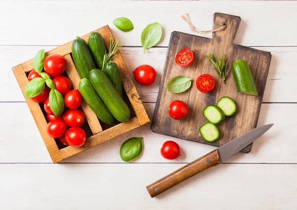 Tomates orgânicos e pepinos com manjericão e toalha de linho em caixa de madeira vintage na mesa de cozinha de madeira. Placa de corte com faca — Fotografia de Stock