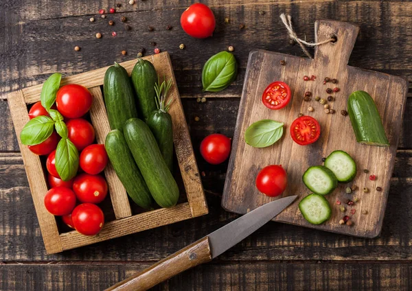 Tomates orgânicos e pepinos com manjericão e toalha de linho em caixa de madeira vintage na mesa de cozinha de madeira. Placa de corte com faca — Fotografia de Stock