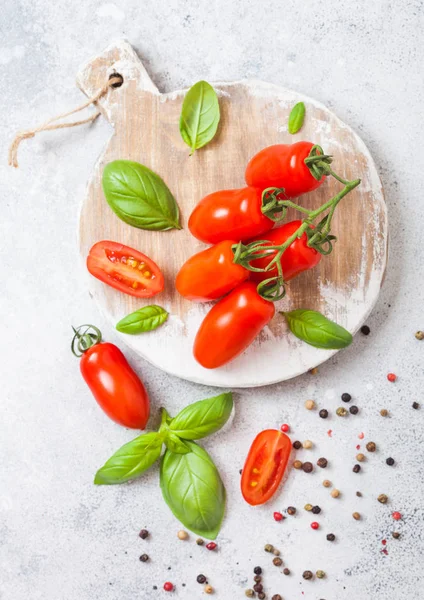 Mini orgânico San Marzano tomates na videira com manjericão e pimenta em tábua de cortar no fundo da cozinha branca . — Fotografia de Stock