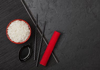 Siyah Chopsticks ve siyah taş arka planda kırmızı keten havlu ile bambu placemat üzerinde tatlı soya sosu ile haşlanmış organik Basmati Yasemin pirinç ile kırmızı kase. Metin alanı