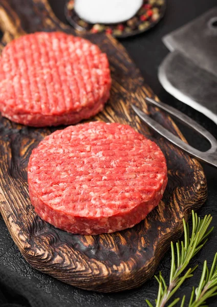 Frisch gehackte hausgemachte Bauern grillen Rindfleisch-Burger auf Vintage-Schneidebrett mit Gewürzen und Kräutern und Fleischbeil, Gabel und Messer auf schwarzem Brett. — Stockfoto