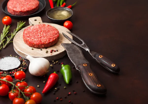 Los agricultores caseros picados crudos frescos asan hamburguesa de carne de res en la tabla de picar redonda con especias y hierbas y tenedor y cuchillo en la tabla marrón. Aceite, pimienta y ajo . —  Fotos de Stock