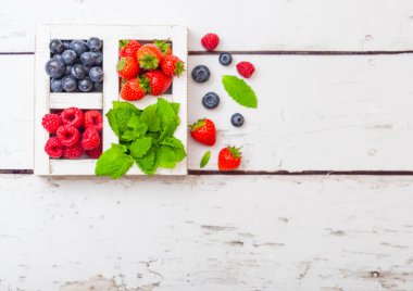 Ahşap arka planda beyaz Vintage ahşap kutu taze ham organik çilek. Metin alanı. Üst görünüm. Çilek, ahududu, yaban mersini ve nane yaprağı