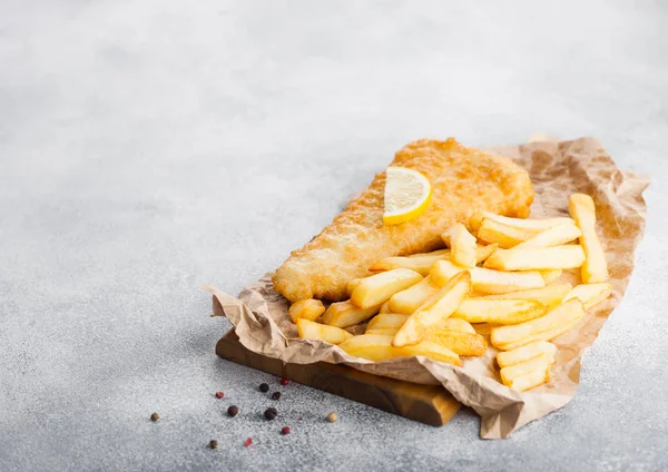 Beyaz taş masa arka planda doğrama tahta üzerinde limon dilim ile geleneksel Ingiliz balık ve cips.