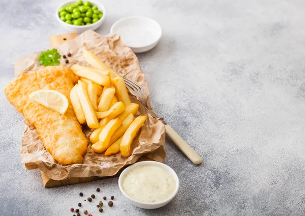 Traditionelle britische Fish and Chips mit Tatarensauce auf Schneidebrett mit Gabel und grünen Erbsen auf weißem Steintischhintergrund. Raum für Text — Stockfoto