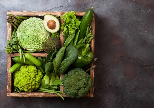 Assorted green toned raw organic vegetables in wooden box on dark background. Avocado, cabbage, cauliflower and cucumber with trimmed and mung beans and pepper and broccoli with sparagus tips. — Stock Photo, Image