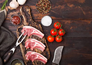 Ahşap arka plan üzerinde vintage et çatal ve bıçak ile doğrama tahtası taze çiğ kasaplar kuzu sığır pirzola. Tuz, biber ve domates ve sarımsak ve barbekü soslu yağ. Metin için alan
