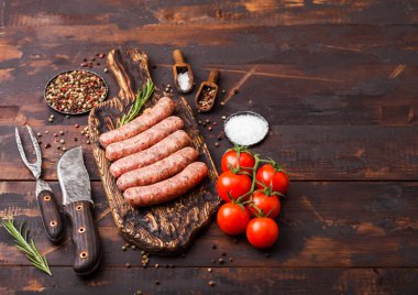 Koyu ahşap arka plan üzerinde vintage bıçak ve çatal ile eski doğrama tahtası üzerinde çiğ sığır eti ve domuz sosis. Biberiye ve domates ile tuz ve biber.