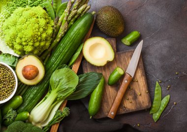 Koyu arka planda ahşap kutuda çeşitli yeşil tonlu ham organik sebzeler. Avokado, lahana, karnabahar ve salatalık ile kesilmiş fasulye ve Doğrama tahtası ile bıçak.