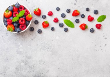 Mutfak masası arka planda beyaz seramik kase plaka taze ham organik çilek. Metin için boşluk. Üst te. Çilek, Ahududu, Yaban Mersini ve Nane yaprağı