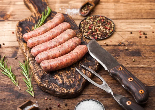 Carne crua e linguiça de porco na velha tábua de cortar com faca vintage e garfo no fundo de madeira.Sal e pimenta com alecrim . — Fotografia de Stock