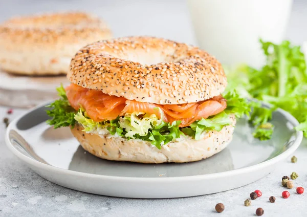 Sanduíche de bagel saudável fresco com salmão, ricota e alface em prato cinza sobre fundo de mesa de cozinha leve. Alimentação saudável. Copo de leite e legumes frescos — Fotografia de Stock