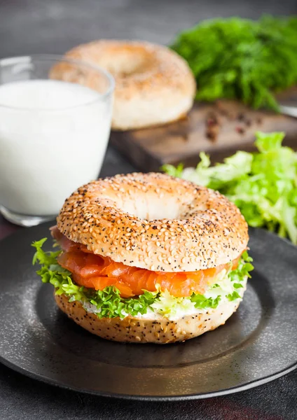 Sanduíche de bagel saudável fresco com salmão, ricota e alface na placa preta no fundo da mesa da cozinha preta. Alimentação saudável. Copo de leite e legumes frescos — Fotografia de Stock