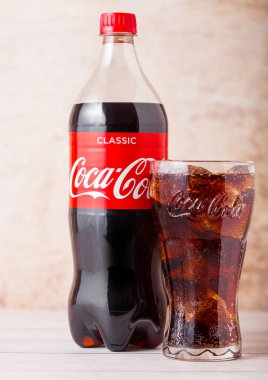 Londra, İngiltere - 03 Ağustos 2018: Ahşap arka planda plastik şişe ve orijinal coca cola meşrubat bardağı. Dünyanın en popüler içkisi.