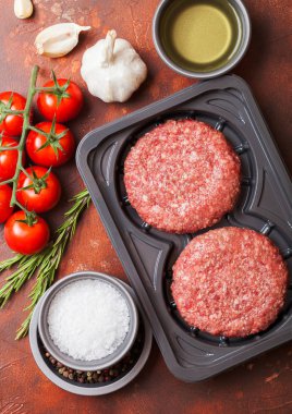 Baharat ve otlar ile çiğ kıyılmış ev yapımı sığır burger ile Plastik tepsi. Üst te. Domates tuz ve biber ile paslı mutfak masa arka plan üzerinde.