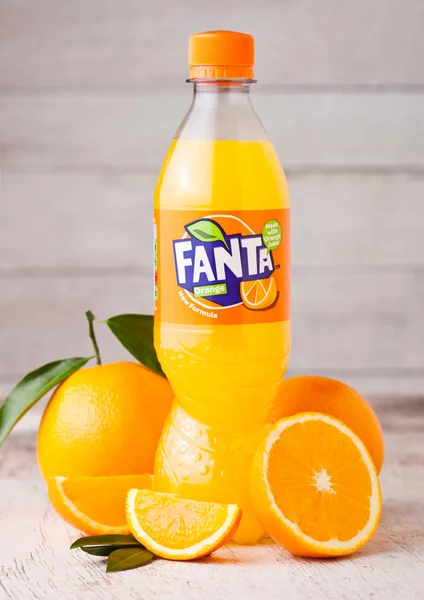 LONDRES, Reino Unido - 31 DE MARZO DE 2018: Botella de plástico de refresco de naranja Fanta sobre fondo de madera clara con naranjas frescas . —  Fotos de Stock