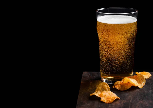 Glas pils bier met aardappel chips snack op vintage houten bord op zwarte achtergrond. Bier en snack. Ruimte voor tekst — Stockfoto