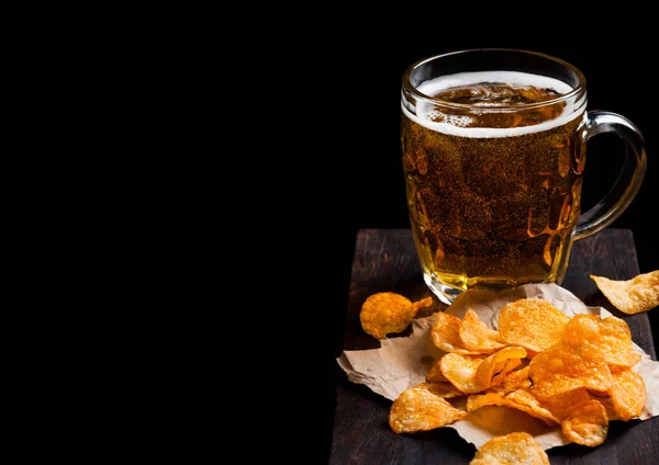 Vaso de cerveza lager con patatas fritas snack en tablero de madera vintage sobre fondo negro. Cerveza y merienda. Espacio para texto — Foto de Stock