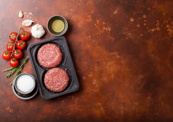 Taca plastikowa z surowego mielonego domowych hamburgery wołowe z przypraw i ziół. Widok z góry i miejsce na tekst na Rusty stół kuchenny tło z pomidorami sól i pieprzem. — Zdjęcie stockowe