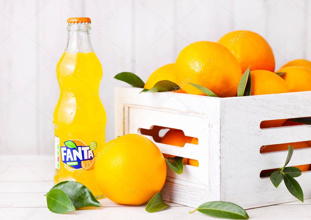 LONDON, UK - MARCH 31, 2018: Glass bottle of Fanta orange soft drink on white wooden background with box of raw oranges.