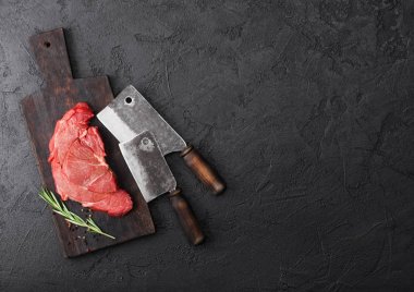 Fresh raw organic slice of braising steak fillet on chopping board with meat hatchets on black stone background. Space for text clipart
