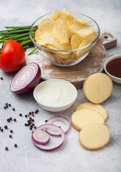 Patatas fritas frescas orgánicas hechas en casa en un tazón de vidrio con crema agria y cebollas rojas sobre un fondo de mesa de cocina claro. Tomate con ketchup y cebolla verde — Foto de Stock