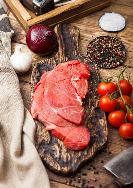 Čerstvý surový organický řez z dušené steak na sekací desce s masovou sekerou na dřevěném podkladu. Červená cibule, rajčata se solí a pepřem. — Stock fotografie