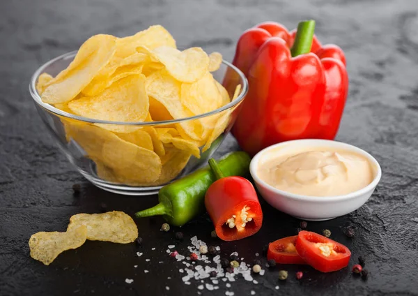 Prato tigela de vidro com batatas fritas batatas fritas com sabor de cebola no fundo da mesa de pedra preta. Pimentos de pimenta vermelha e verde com páprica e molho picante quente . — Fotografia de Stock