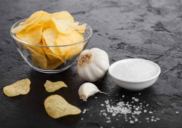 Placa de vidrio con patatas fritas con sabor a cebolla con ajo y sal sobre fondo de mesa de piedra negra . — Foto de Stock