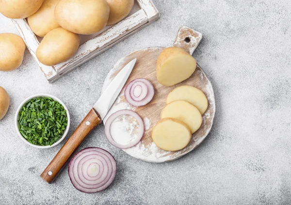 Patatas frescas orgánicas crudas en caja de madera y sobre tabla de cortar con cebollas rojas y verdes sobre fondo de mesa claro . — Foto de Stock