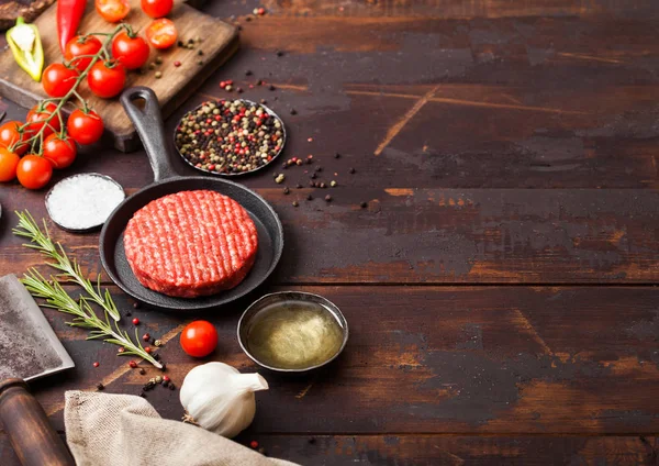 Los granjeros caseros picados crudos frescos asan hamburguesa de carne de res en una sartén con especias y hierbas y hacha de carne en un tablero de madera. Aceite, ajo y tomates . — Foto de Stock