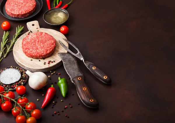 Los agricultores caseros picados crudos frescos asan hamburguesa de carne de res en la tabla de picar redonda con especias y hierbas y tenedor y cuchillo en la tabla marrón. Aceite, pimienta y ajo . —  Fotos de Stock