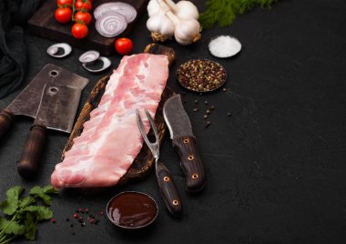 Siyah taş zemin üzerine kurulu ve vintage et çatalı ve bıçağı doğrama üzerinde taze çiğ Domuz kaburga. Taze domates ve kırmızı soğan sarımsak, tuz ve biber ile. Metin için yer