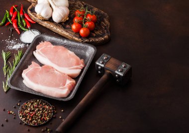 Tuz ve karabiber ve vintage et baltaları ve paslı arka plan üzerinde çekiç ile plastik tepsi içinde çiğ domuz loin pirzola. Kırmızı biber, domates ve sarımsak. 