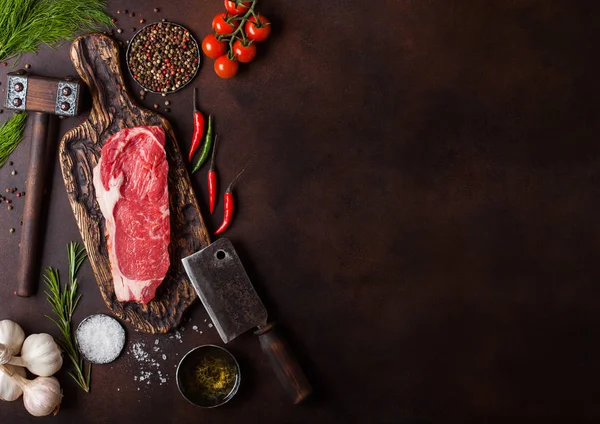 Raw sirloin beef steak on old chopping board with salt and pepper and vintage meat hatchets and hammer on rusty background.Red pepper, tomatoes and garlic. Space for text — Stock Photo, Image