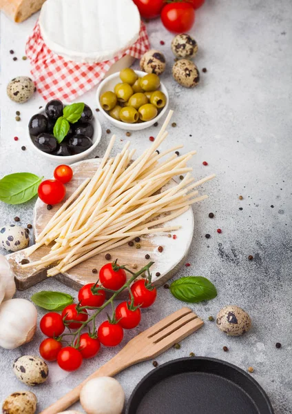 Homemade spaghetti pasta with quail eggs with bottle of tomato sauce and cheese on kitchen background. Classic italian village food. Garlic, champignons, black and green olives, pan and spatula. — Stock Photo, Image